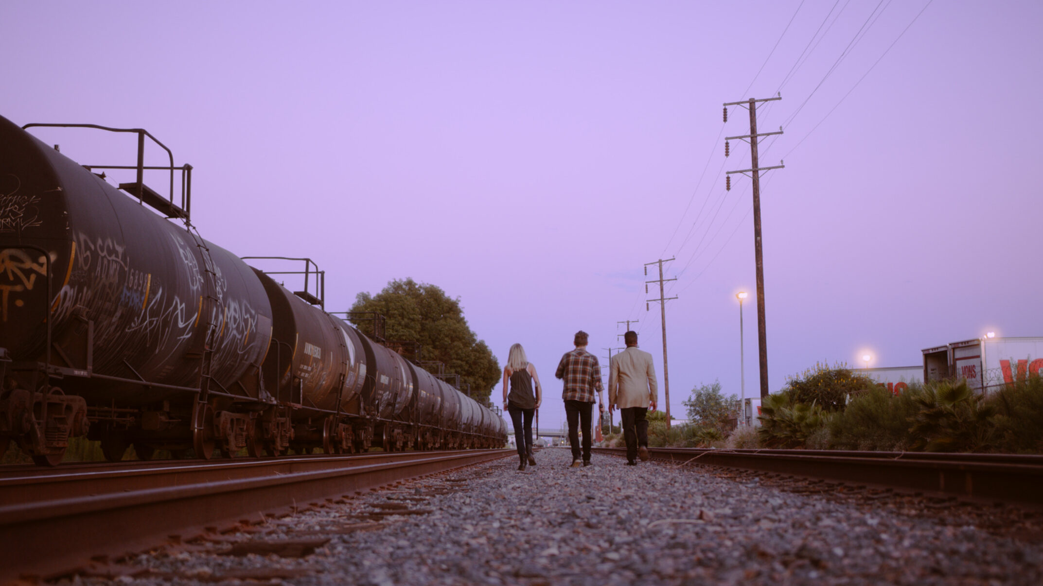 three people walking next to a stopped train at sunset in Trap Door at the Edge of the Universe